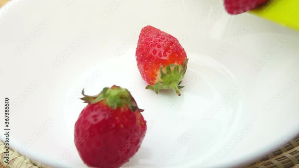 Close-up of large juicy strawberries falling into the white bowl in slow motion Close-up of large juicy strawberries falling into the white bowl in slow motion