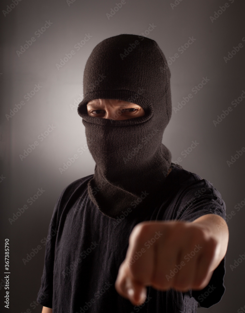 angry man in a balaclava on a dark background. Rebellious protester in a mask shows his fist. angry man in a balaclava on a dark background. Rebellious protester in a mask shows his fist.