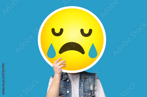 Bild auf Leinwand Unrecognizable man hiding his face behind crying sad emoticon emoji