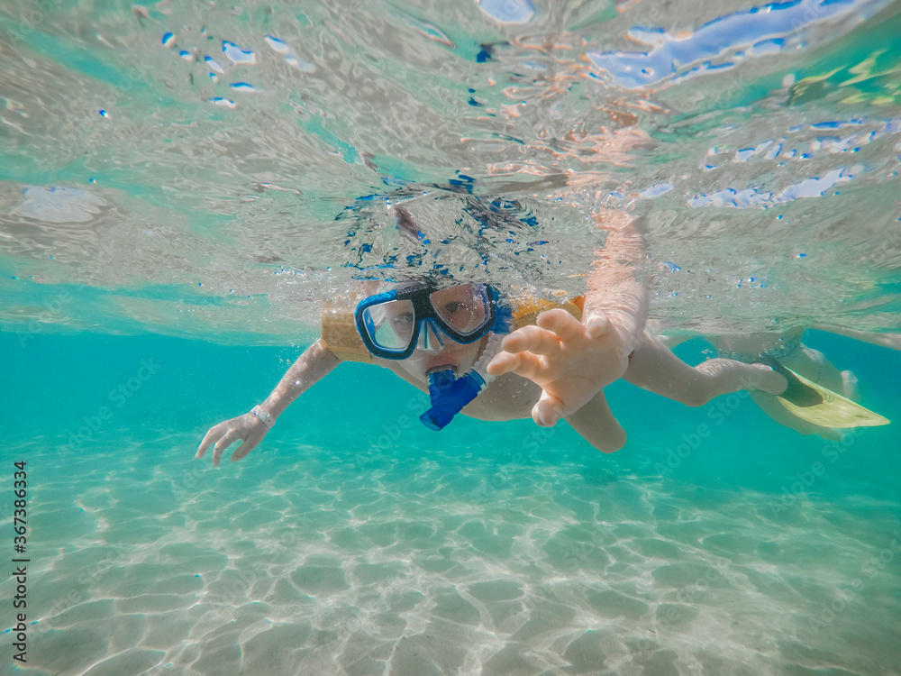 Underwater picture of boy in mask and flippers with blue water and sand coastline. Summertime activity. Snorkeling to see underwater life. Holidays for kids in the sea vacation in tropical country. 
