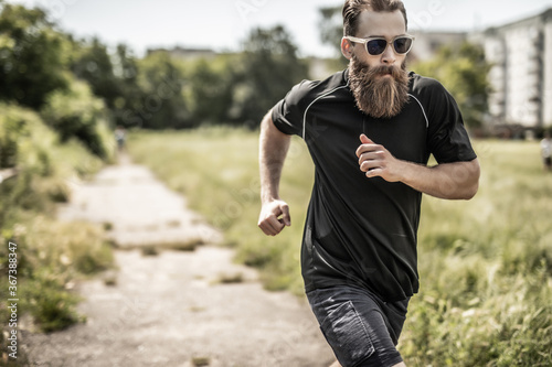 Young happy cheerful smiling bearded man, during morning jogging outdoors. Fitness, sport, exercising, crossfit and workout concept.