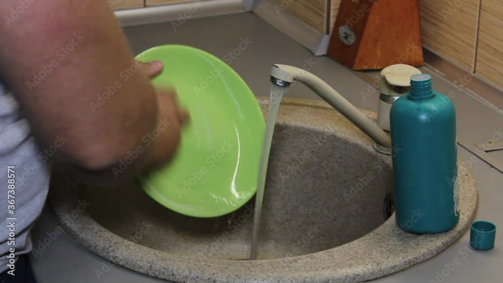 Male hands washes the dishes in the kitchen sink. A person doing household chores. Wash the green plate with a kitchen washcloth. Soapy foam and bubbles. Male hands washes the dishes in the kitchen sink. A person doing household chores. Wash the green plate with a kitchen washcloth. Soapy foam and bubbles.