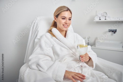 Happy young woman drinking glass of water in spa salon