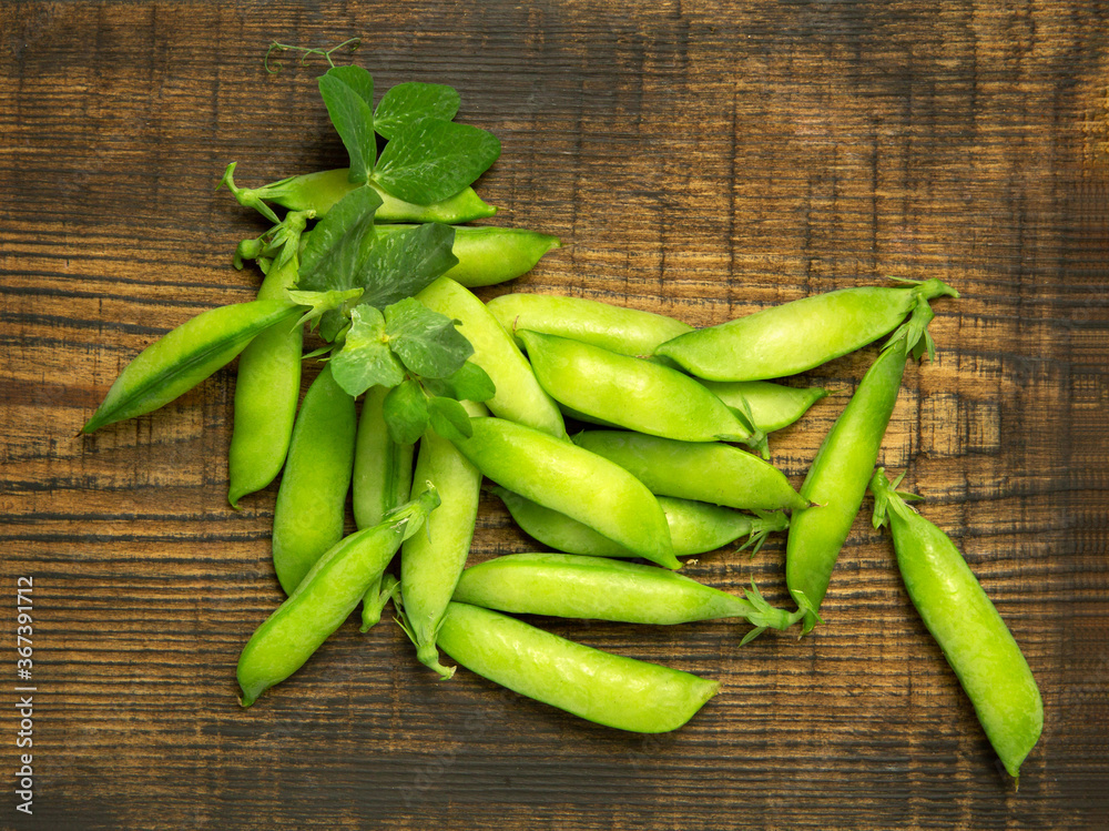 Pods of green peas with leaves on a wooden brown background. Flat lay. Food, diet, vegetarianism, vitamins. Pods of green peas with leaves on a wooden brown background. Flat lay. Food, diet, vegetarianism, vitamins.