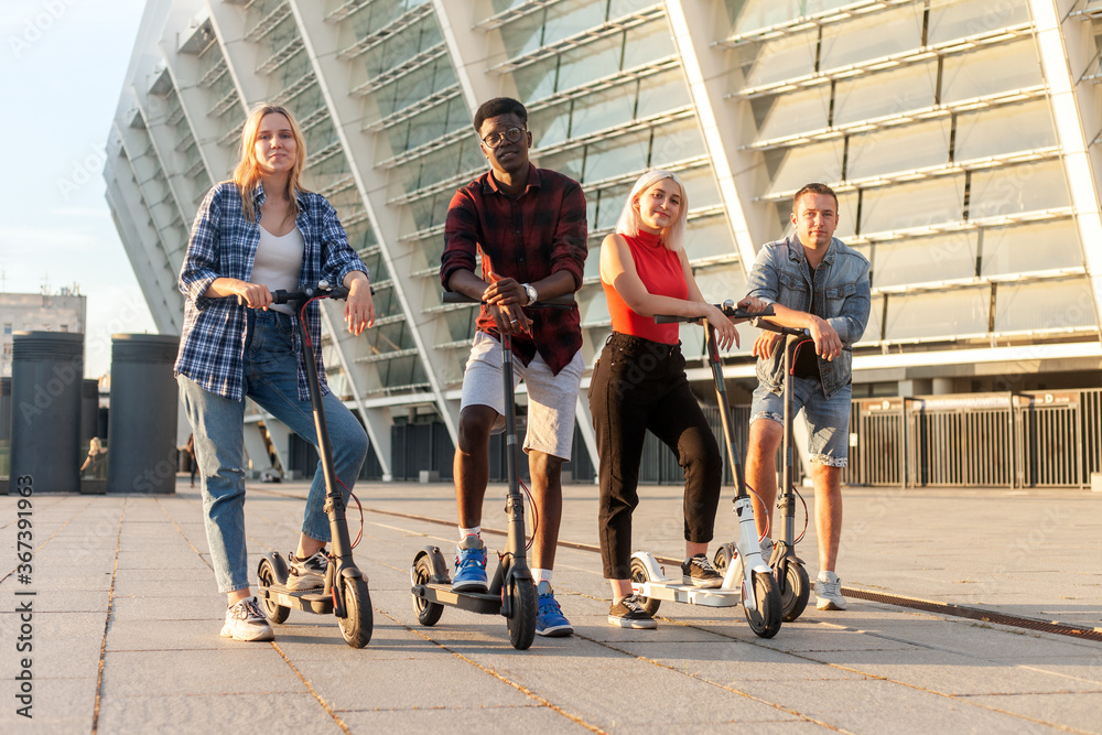 interracial group of friends ride electric scooters in the city, multiracial youth use electric vehicles