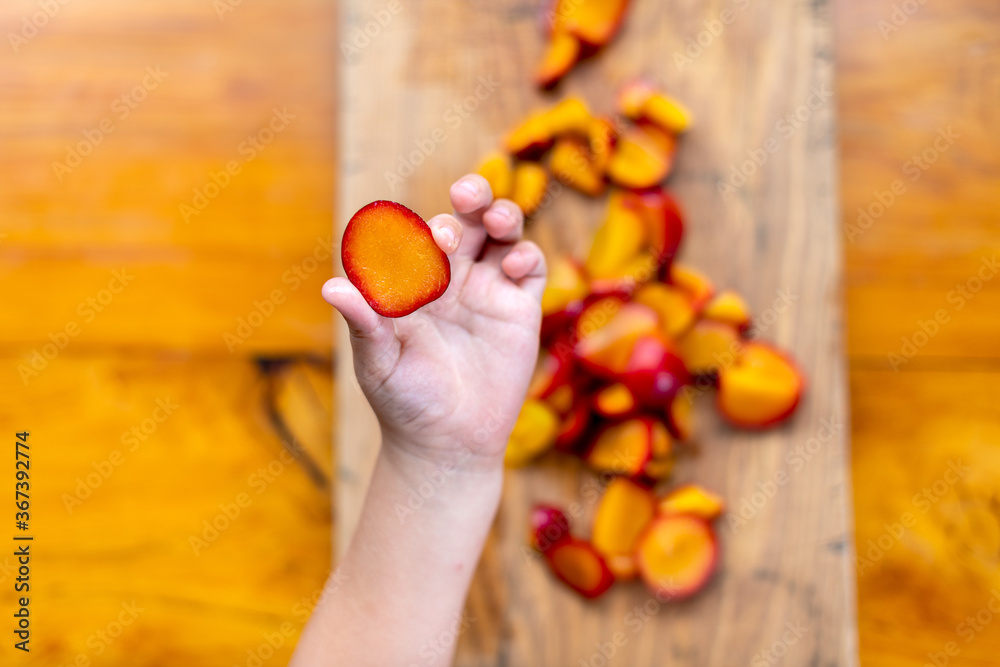 Close up of a child's hand holding an slice of fruit with remainder of fresh fruit on wooden board in background Close up of a child's hand holding an slice of fruit with remainder of fresh fruit on wooden board in background