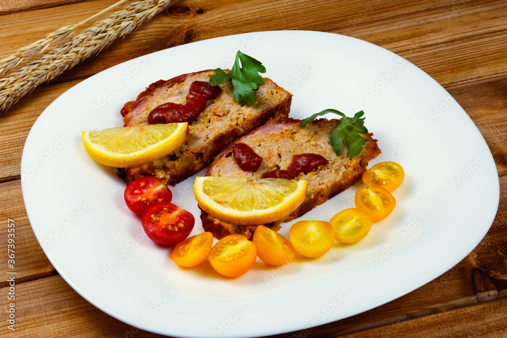 Classic meatloaf, cherry tomatoes, lemon wedge, parsley in a white plate on a wooden background. Ears of wheat Classic meatloaf, cherry tomatoes, lemon wedge, parsley in a white plate on a wooden background. Ears of wheat