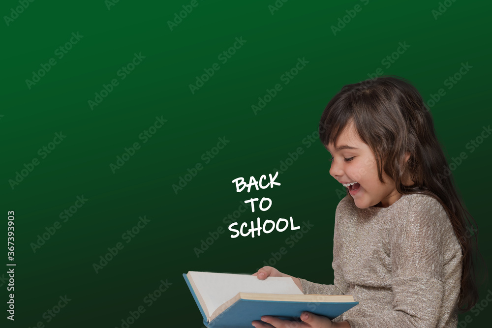 Φωτογραφία Laughing long haired tanned little girl is holding a book, from which the inscription Back to School fly out