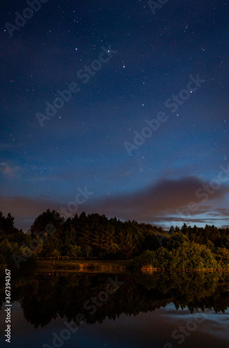 Evening landscape: Ursa major constellation and first stars and a comet Neowise over a forest lake just after sunset. Long exposure night landscape. 