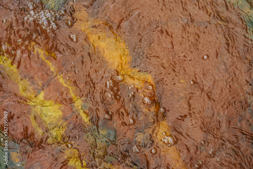 Colorful nature background of yellow red clay bottom. Natural texture of multicolored clay in clear water of mountain creek. Red yellow sandy bottom of mountain river. Full frame of ripples on water.