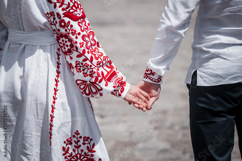 Newlyweds hold hands, dressed in red embroidery