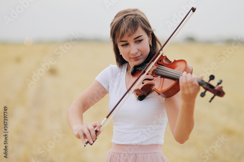 Beautiful romantic girl with loose hair playing the violin in the field.