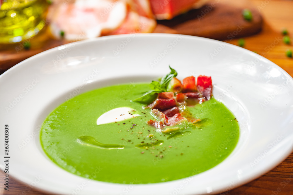 Green pea cream soup with bacon in white plate. Close up Green pea cream soup with bacon in white plate. Close up