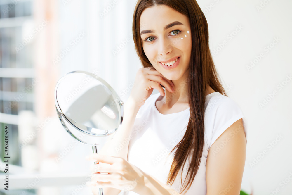 Facial skin care, young woman applies face cream in the spacious bathroom of a luxury hotel with panoramic park views Facial skin care, young woman applies face cream in the spacious bathroom of a luxury hotel with panoramic park views