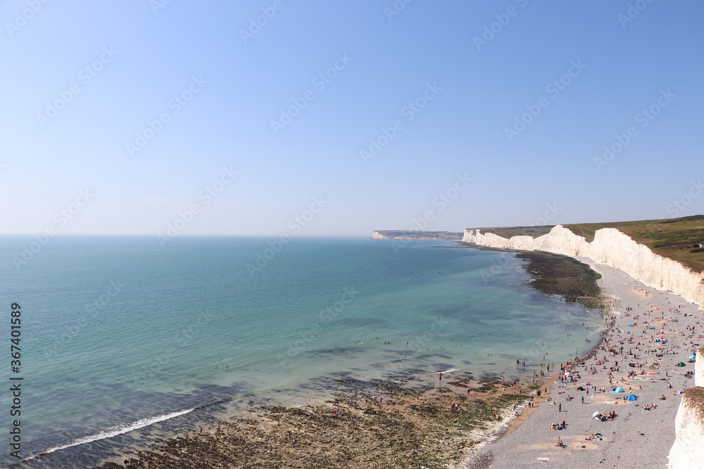 large white rocks by the ocean and blue sky, beach with relax people and green meadows