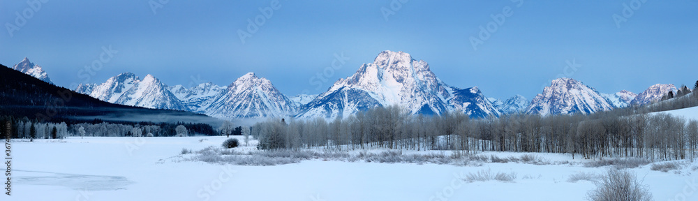 Wide panorama of mist over Oxbow Bend at sunrise on the Snake River with Grand Teton Peaks and Mount Moran on a cold winter morning