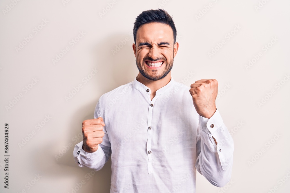 Young handsome man with beard wearing casual t-shirt standing over white background celebrating surprised and amazed for success with arms raised and eyes closed Young handsome man with beard wearing casual t-shirt standing over white background celebrating surprised and amazed for success with arms raised and eyes closed
