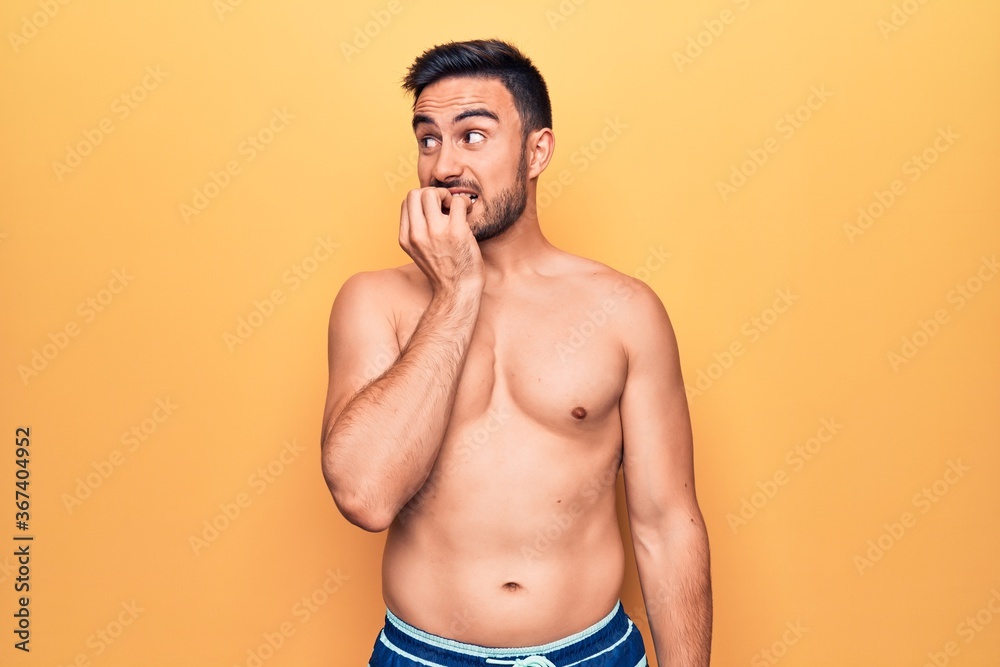 Young handsome man with beard wearing sleeveless t-shirt standing over yellow background looking stressed and nervous with hands on mouth biting nails. Anxiety problem.