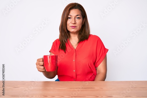 Obraz na plátně Middle age brunette woman drinking a cup of coffee sitting on the table thinking