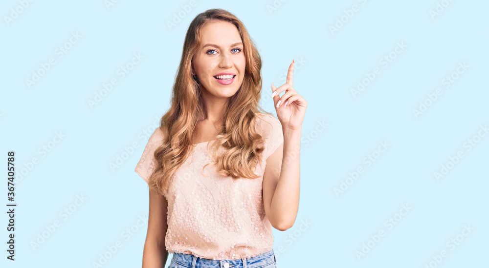 Young beautiful caucasian woman with blond hair wearing casual clothes pointing finger up with successful idea. exited and happy. number one. Young beautiful caucasian woman with blond hair wearing casual clothes pointing finger up with successful idea. exited and happy. number one.
