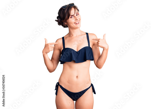 Beautiful young woman with short hair wearing bikini looking confident with smile on face, pointing oneself with fingers proud and happy.