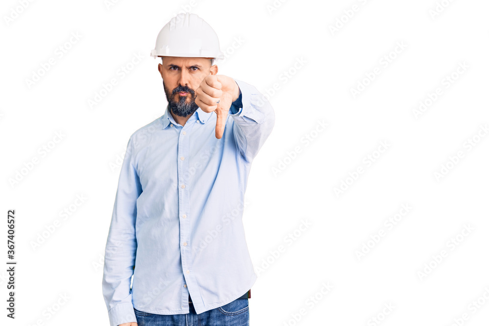 Young handsome man wearing architect hardhat looking unhappy and angry showing rejection and negative with thumbs down gesture. bad expression.