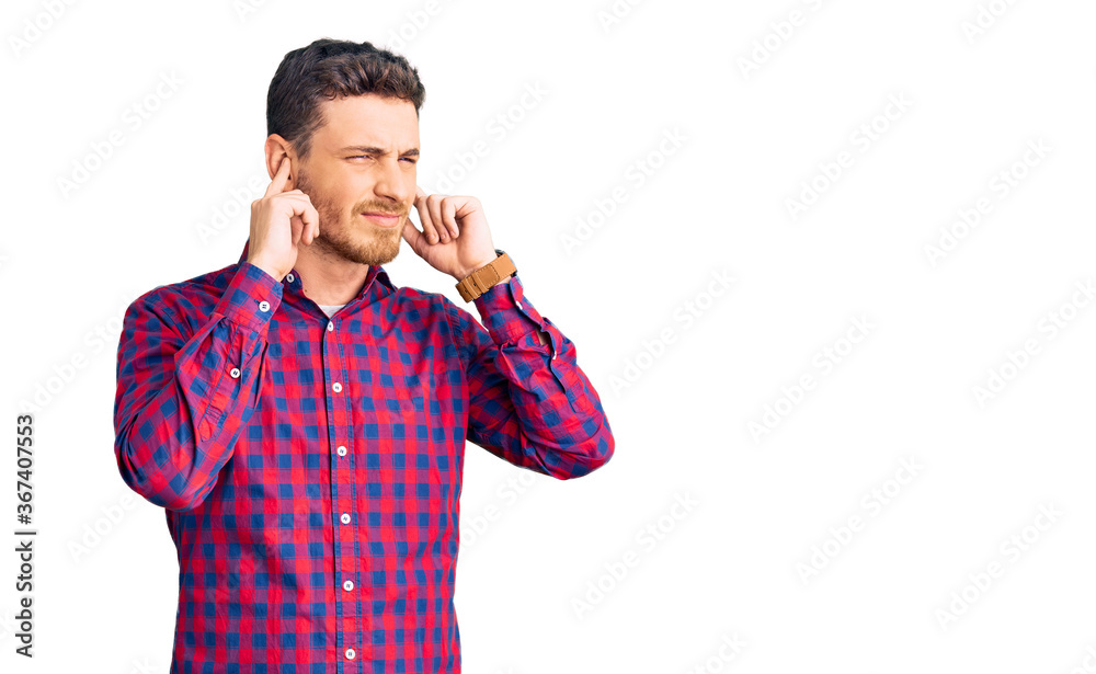 Handsome young man with bear wearing casual shirt covering ears with fingers with annoyed expression for the noise of loud music. deaf concept. Handsome young man with bear wearing casual shirt covering ears with fingers with annoyed expression for the noise of loud music. deaf concept.