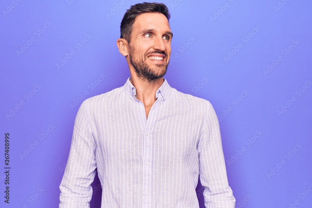 Young handsome man wearing casual striped shirt standing over isolated purple background looking to side, relax profile pose with natural face and confident smile. Young handsome man wearing casual striped shirt standing over isolated purple background looking to side, relax profile pose with natural face and confident smile.