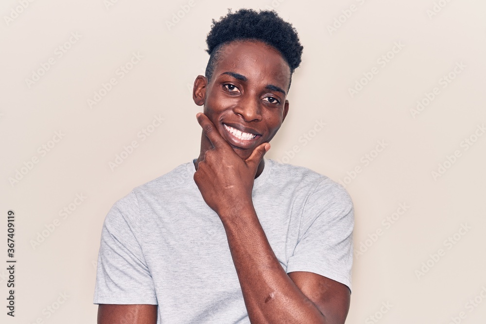 Young african american man wearing casual clothes looking confident at the camera smiling with crossed arms and hand raised on chin. thinking positive. Young african american man wearing casual clothes looking confident at the camera smiling with crossed arms and hand raised on chin. thinking positive.