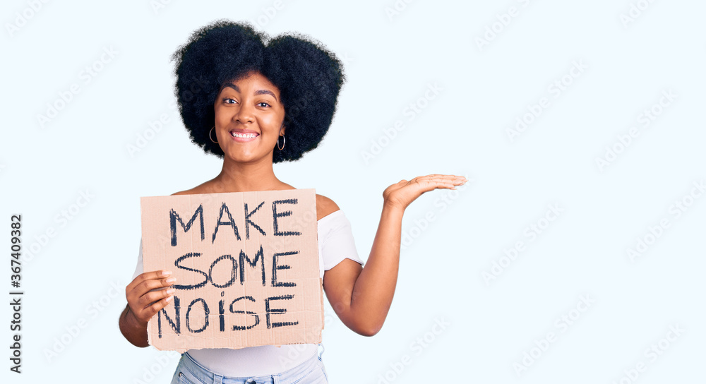 Young african american girl holding make some noise banner celebrating victory with happy smile and winner expression with raised hands Young african american girl holding make some noise banner celebrating victory with happy smile and winner expression with raised hands