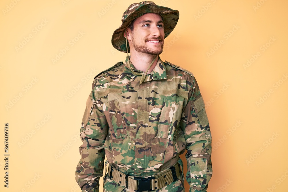 Young caucasian man wearing camouflage army uniform looking away to side with smile on face, natural expression. laughing confident. Young caucasian man wearing camouflage army uniform looking away to side with smile on face, natural expression. laughing confident.