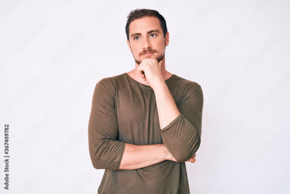Young handsome man wearing casual clothes with hand on chin thinking about question, pensive expression. smiling with thoughtful face. doubt concept. Young handsome man wearing casual clothes with hand on chin thinking about question, pensive expression. smiling with thoughtful face. doubt concept.