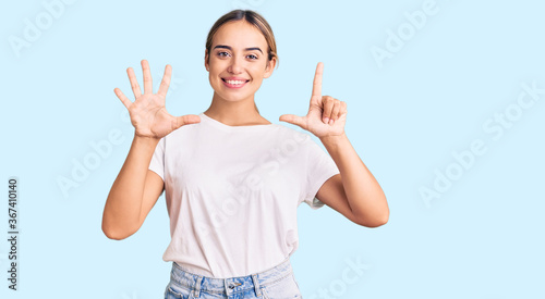 Young beautiful blonde woman wearing casual white tshirt showing and pointing up with fingers number seven while smiling confident and happy.