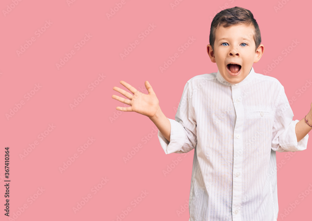 Cute blond kid wearing elegant shirt celebrating crazy and amazed for success with arms raised and open eyes screaming excited. winner concept