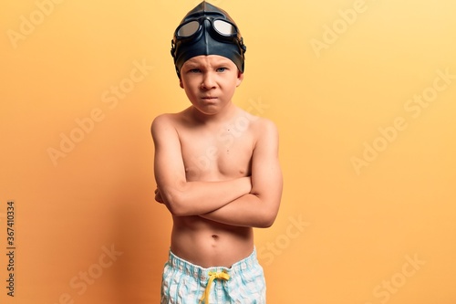 Cute blond kid wearing swimwear and swimmer glasses skeptic and nervous, disapproving expression on face with crossed arms. negative person. © Krakenimages.com