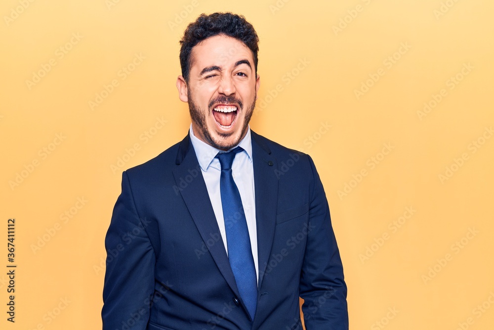 Young hispanic man wearing suit winking looking at the camera with sexy expression, cheerful and happy face. Young hispanic man wearing suit winking looking at the camera with sexy expression, cheerful and happy face.
