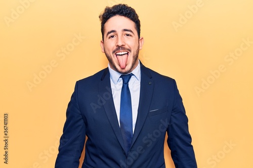 Young hispanic man wearing suit sticking tongue out happy with funny expression. emotion concept.