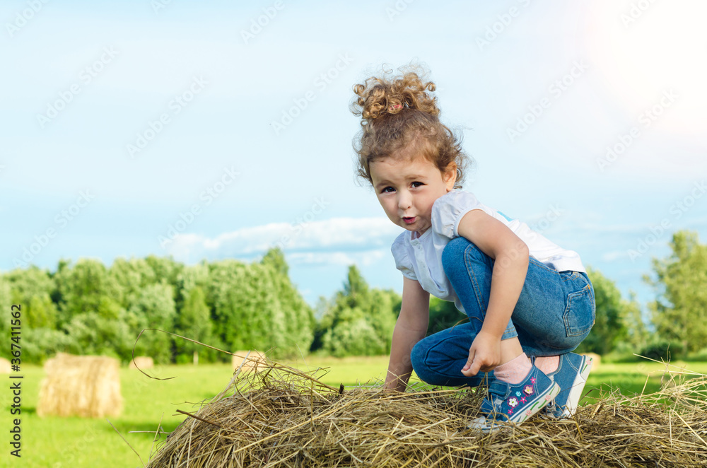 little beautiful girl on the field, on roll haystack. child plays during haymaking. childhood. harvesting, oktoberfest. little beautiful girl on the field, on roll haystack. child plays during haymaking. childhood. harvesting, oktoberfest.