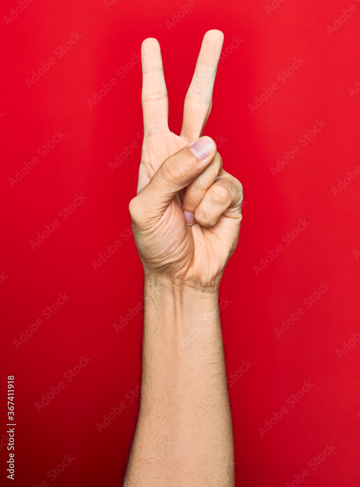 Beautiful hand of man showing two fingers up doing victory sign over isolated red background Beautiful hand of man showing two fingers up doing victory sign over isolated red background