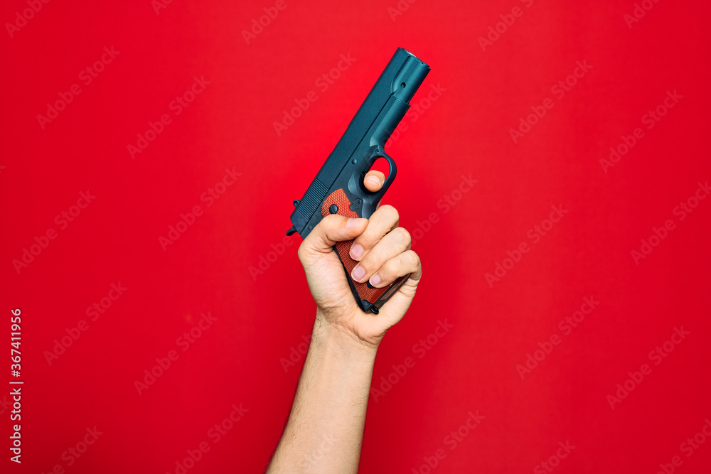 Beautiful hand of man holding gun over isolated red background Beautiful hand of man holding gun over isolated red background