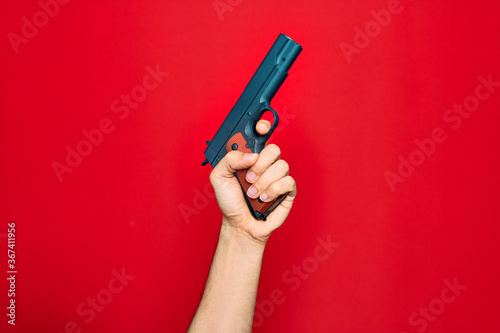 Beautiful hand of man holding gun over isolated red background