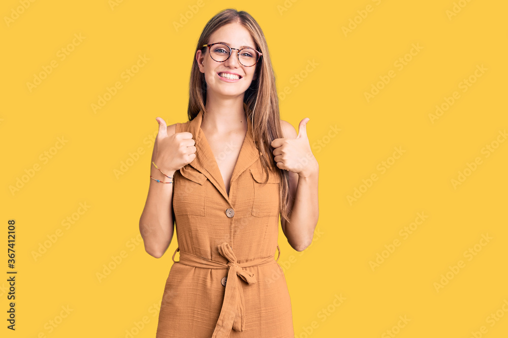 Young beautiful blonde woman wearing casual clothes and glasses success sign doing positive gesture with hand, thumbs up smiling and happy. cheerful expression and winner gesture.