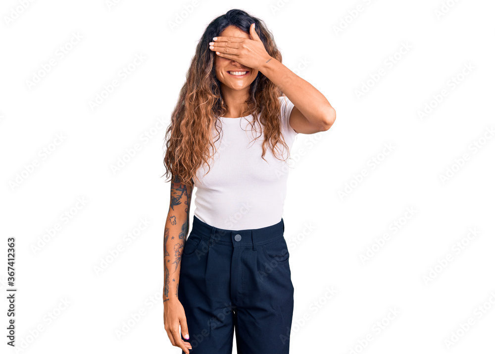 Young hispanic woman with tattoo wearing casual white tshirt smiling and laughing with hand on face covering eyes for surprise. blind concept. Young hispanic woman with tattoo wearing casual white tshirt smiling and laughing with hand on face covering eyes for surprise. blind concept.