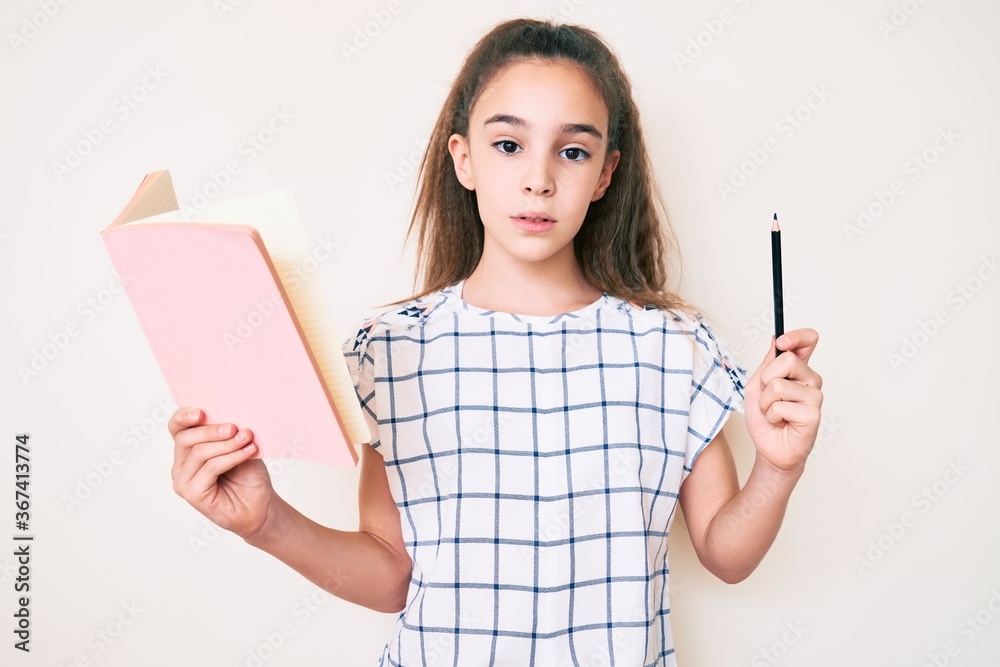 Cute hispanic child girl holding book and pencil thinking attitude and sober expression looking self confident Cute hispanic child girl holding book and pencil thinking attitude and sober expression looking self confident
