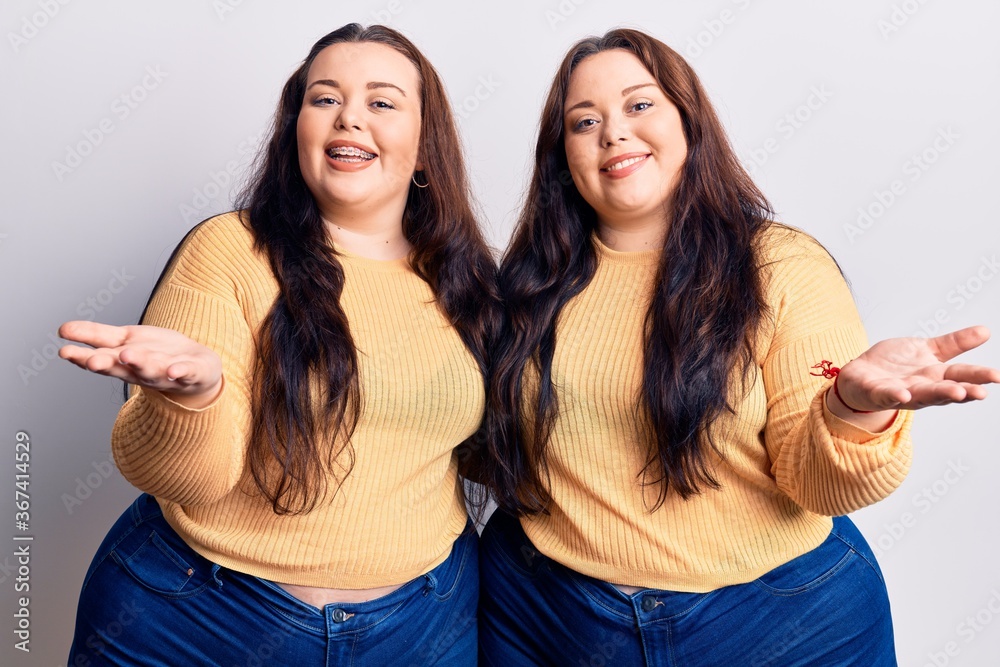 Young plus size twins wearing casual clothes smiling cheerful offering hands giving assistance and acceptance. Young plus size twins wearing casual clothes smiling cheerful offering hands giving assistance and acceptance.