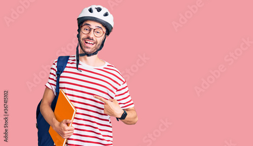 Young hispanic man wearing student backpack and bike helmet holding binder smiling happy pointing with hand and finger