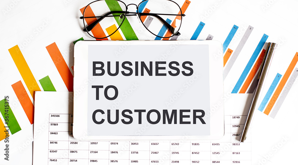 The tablet with text BUSINESS TO CUSTOMER on business charts and pen The tablet with text BUSINESS TO CUSTOMER on business charts and pen