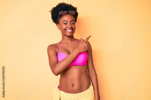 Young african american woman wearing bikini cheerful with a smile of face pointing with hand and finger up to the side with happy and natural expression on face © Krakenimages.com