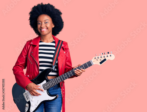 Young african american woman playing electric guitar looking positive and happy standing and smiling with a confident smile showing teeth