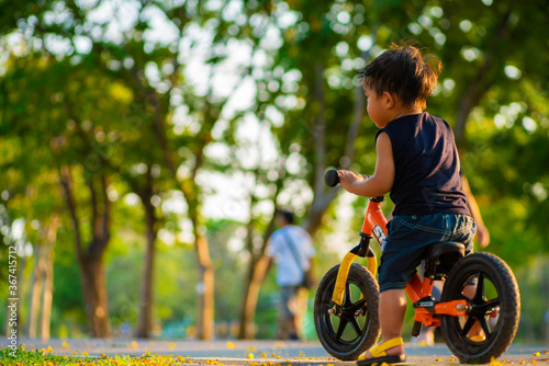Little boy ride balance bike on road in city public tree park